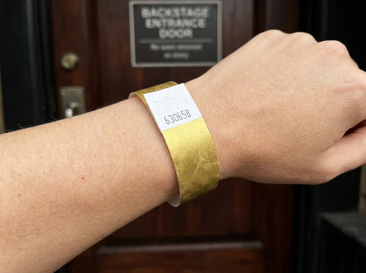 VIP-Festivalarmband mit goldenem Metallic-Aufdruck und Barcode, getragen an einem Handgelenk vor einem Backstage-Eingang
