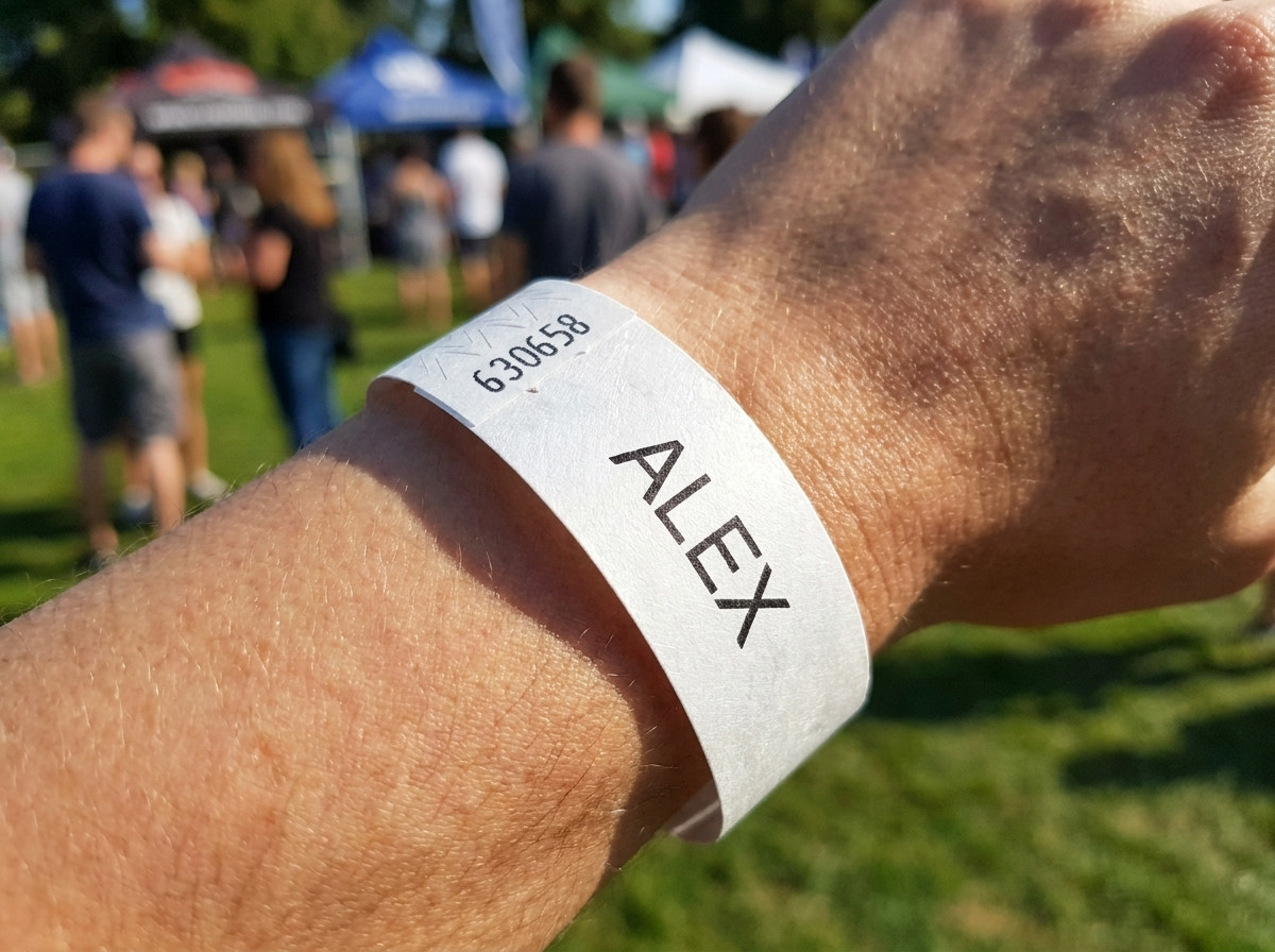 Weisses Tyvek-Armband mit aufgedrucktem Vornamen eines Kindes und Notfalltelefonnummer, getragen am Handgelenk eines Kleinkindes bei einer Veranstaltung im Freien